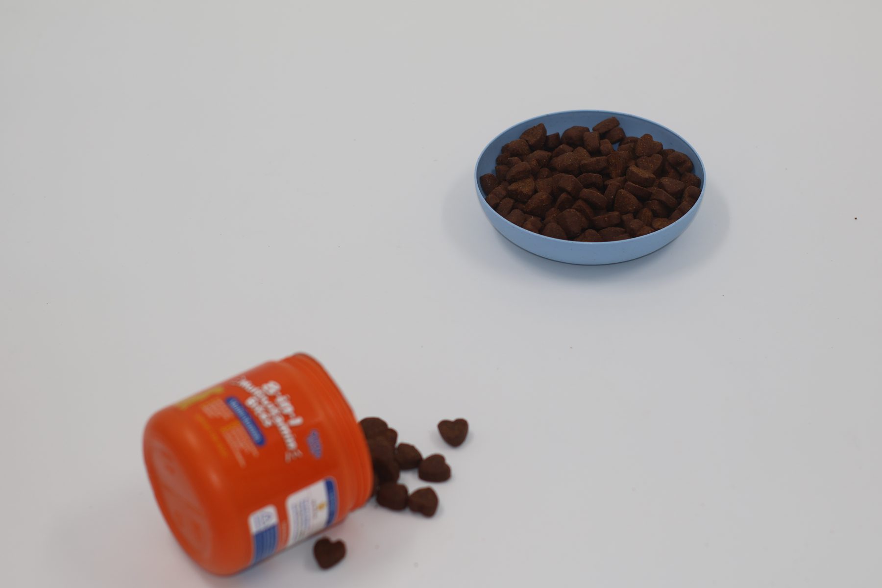 8-in-1 jar on its side with heart chews spilled. A formed, palatable matrix, not a biscuit and not a gummy